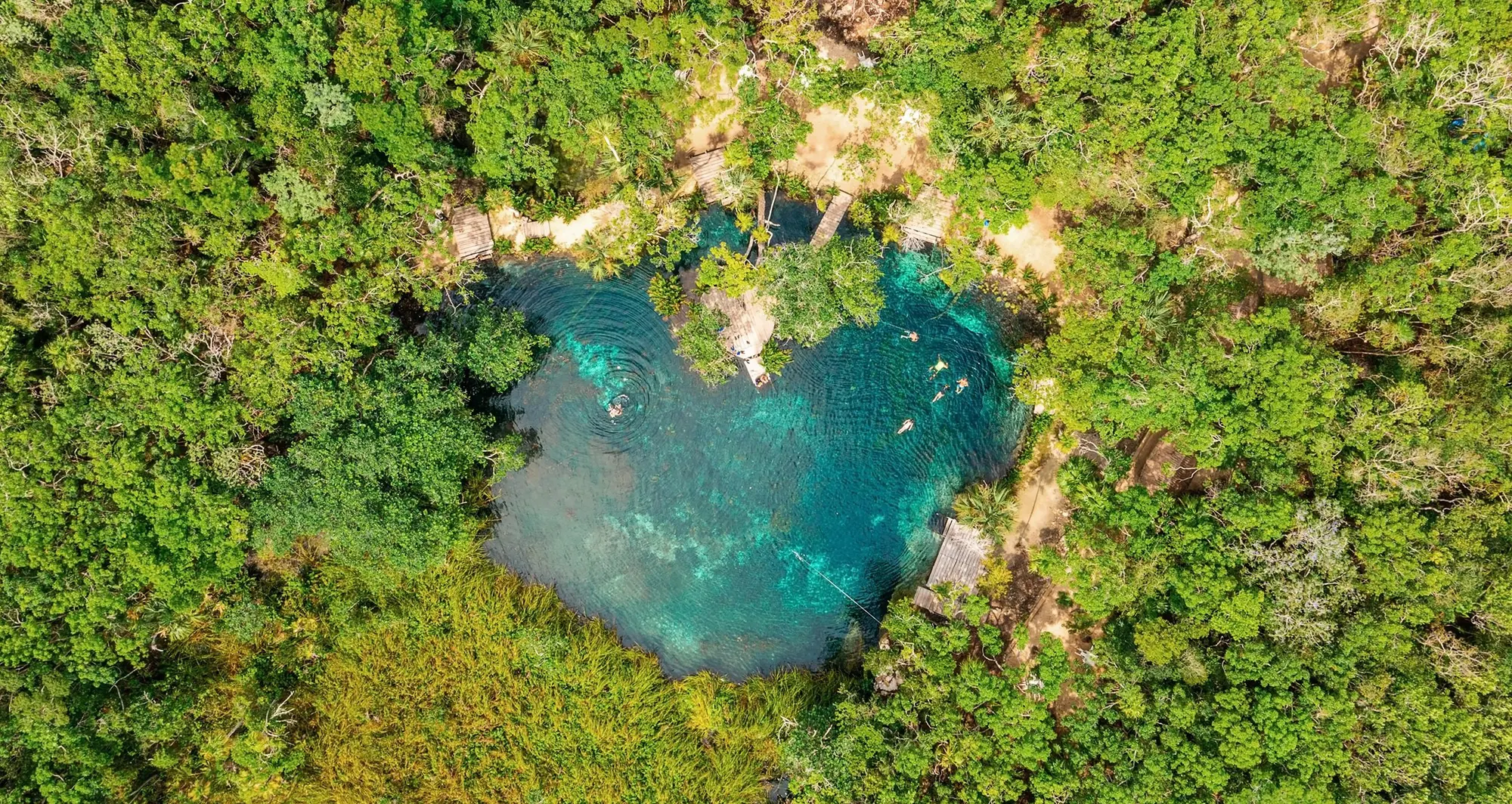 Vista aérea de um cenote de águas cristalinas cercado pela selva na região de Tulum